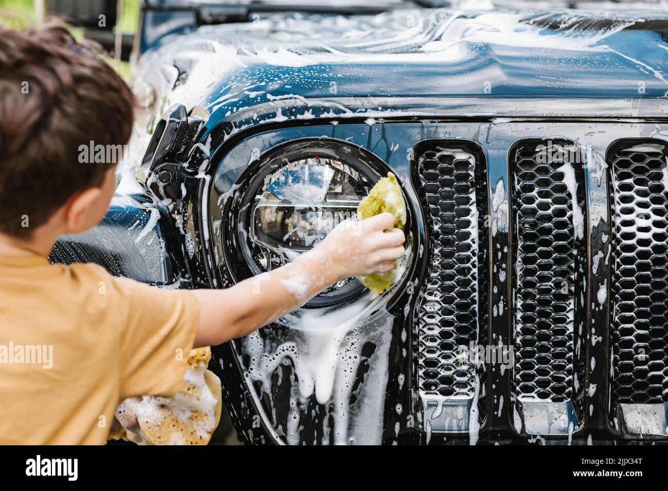 Back view of boy cleaning black car with sponge and soap Stock Photo