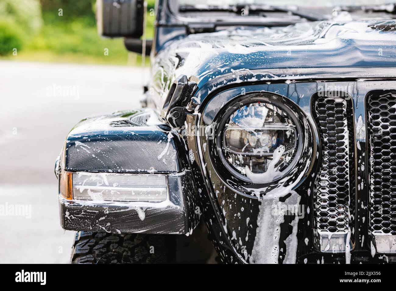 Front view of black car covered with washing foam and soap bubble on