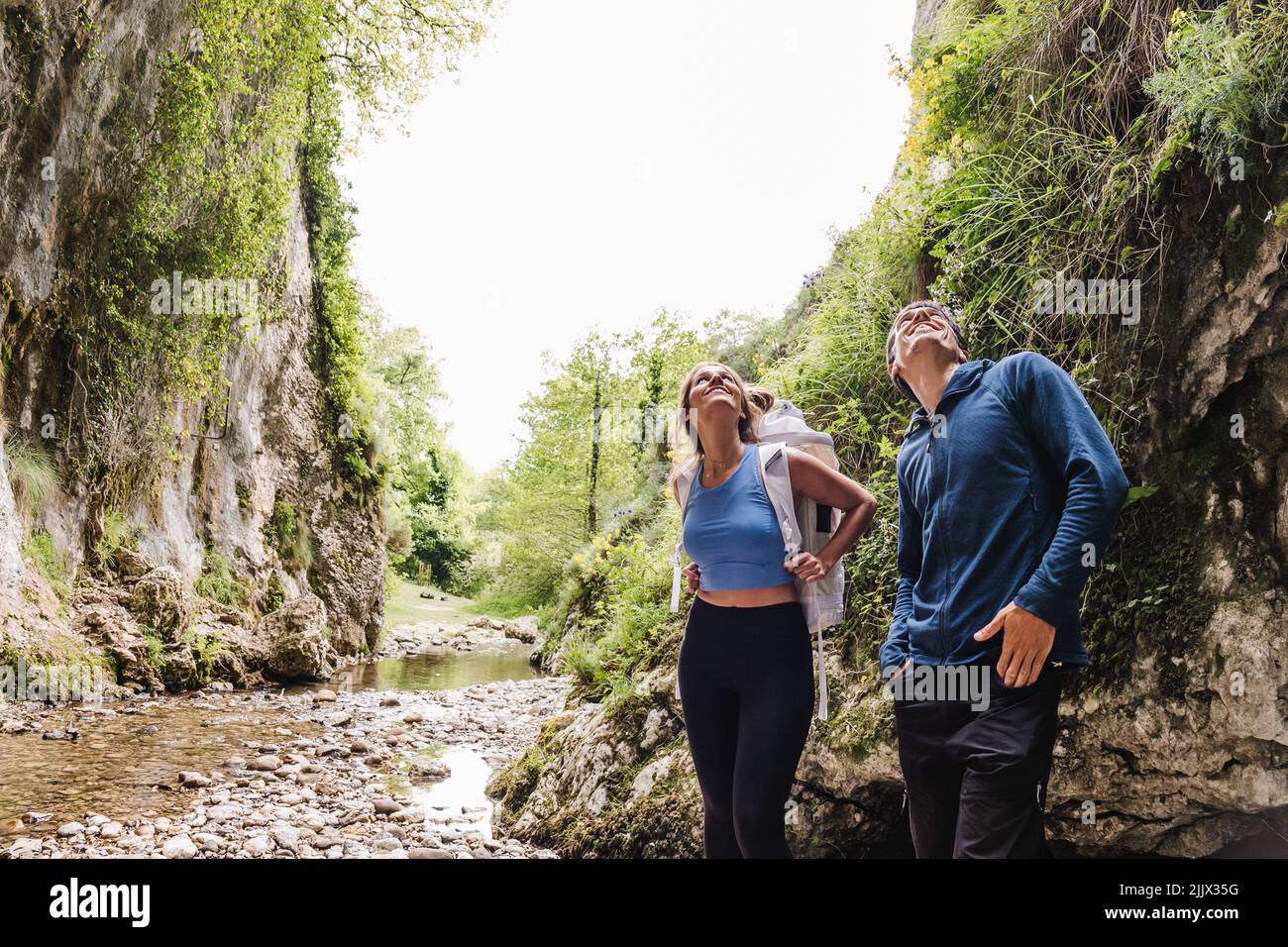 Smiling couple looking up while standing by cliff in forest Stock Photo