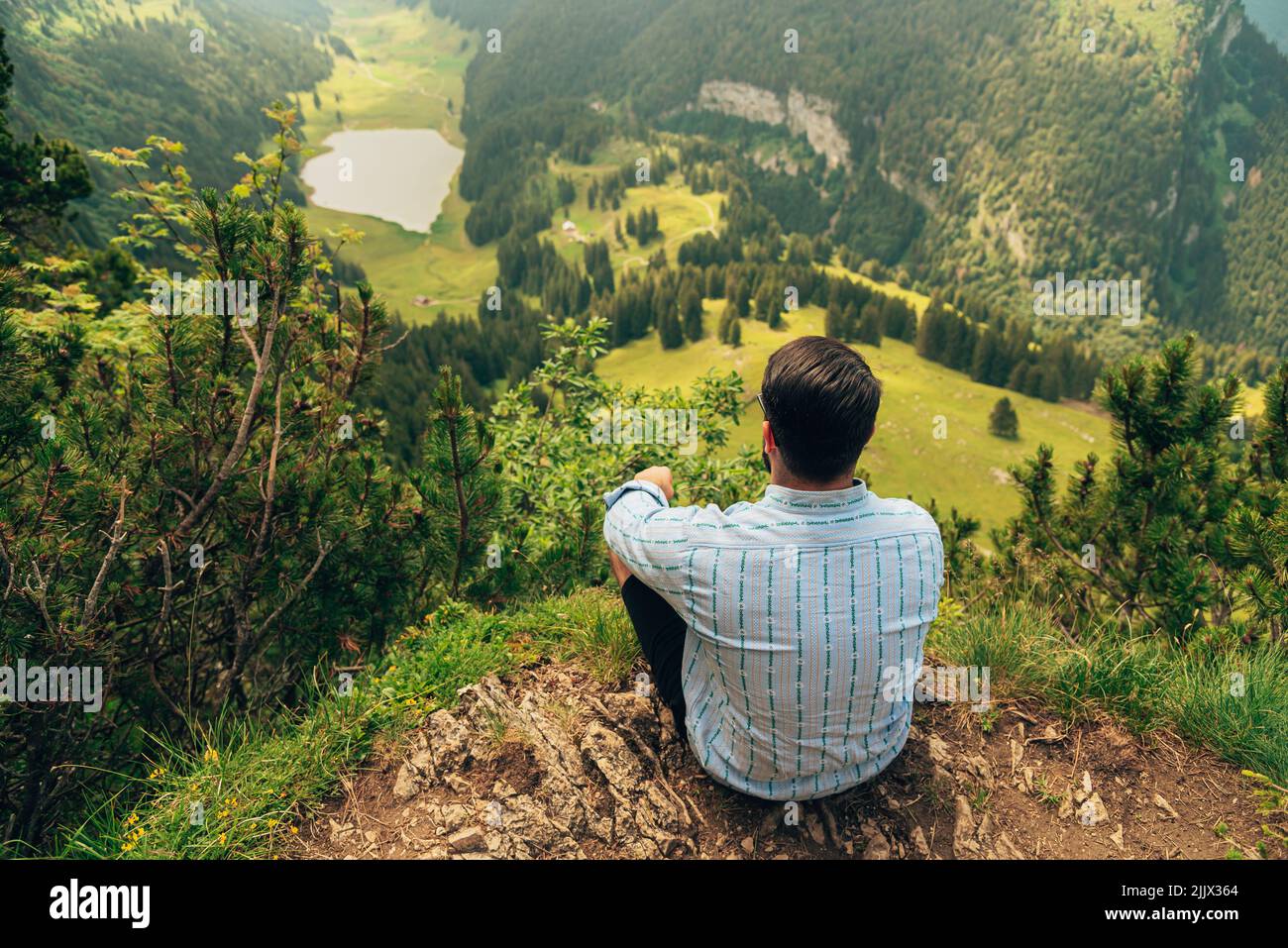 A man sitting on a hill overlooking a vast landscape in the countryside of Appenzell, Switzerland Stock Photo