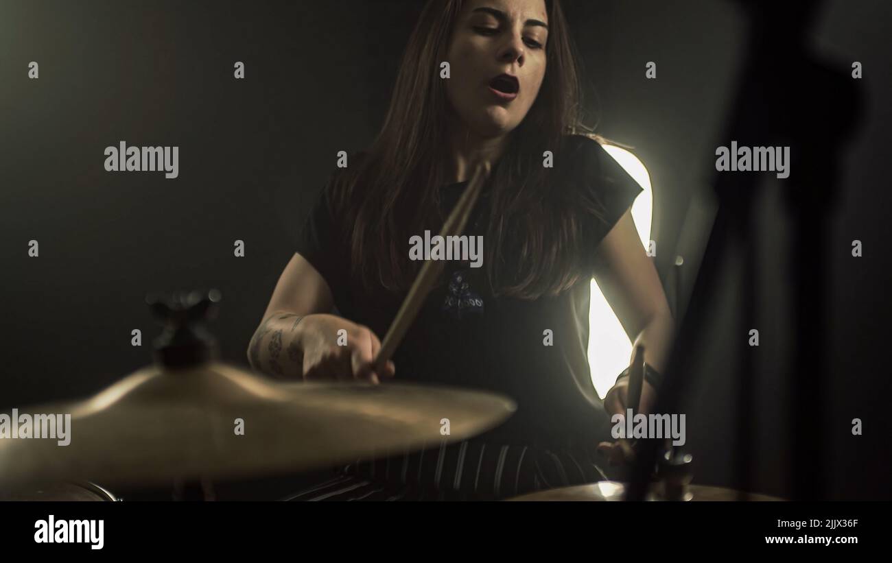An energetic female drummer plays the drum kit holding drumsticks in her hands Stock Photo