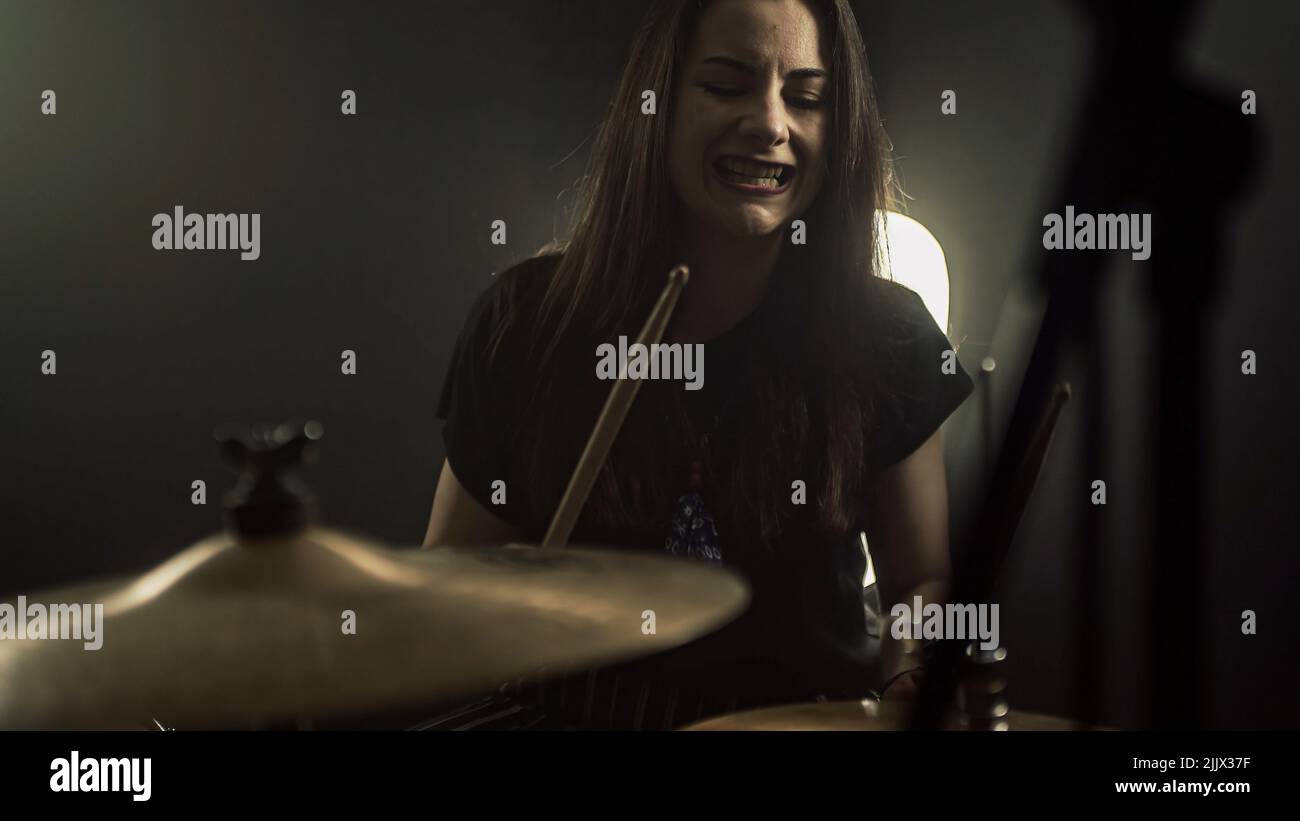 An energetic female drummer plays the drum kit holding drumsticks in her hands Stock Photo