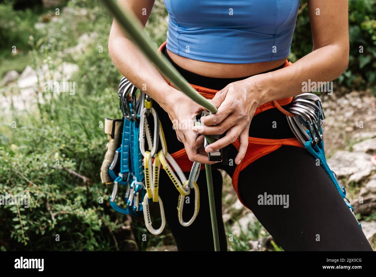 Midsection of female hiker tying rope on harness while preparing for