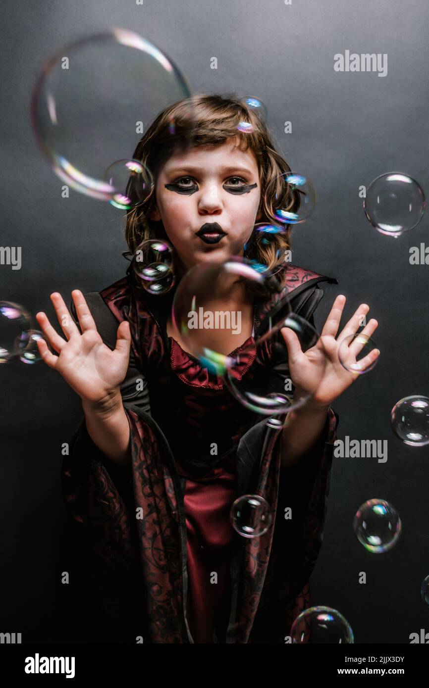 Adorable little girl with dark makeup in witch costume pouting lips and