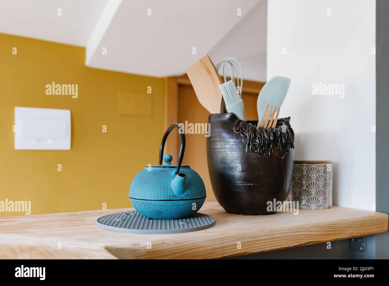 Blue cast iron teapot and vase with kitchen utensils placed on wooden counter in modern