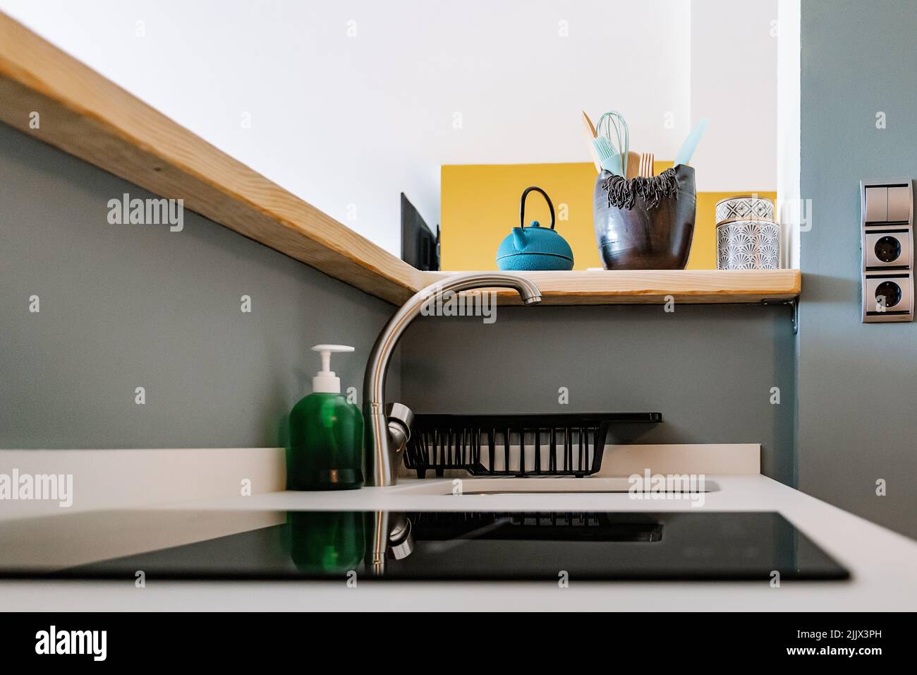 Iron teapot and bowl with utensils placed on wooden counter over sink with chrome faucet and built in stove in modern kitchen in daylight Stock Photo Alamy