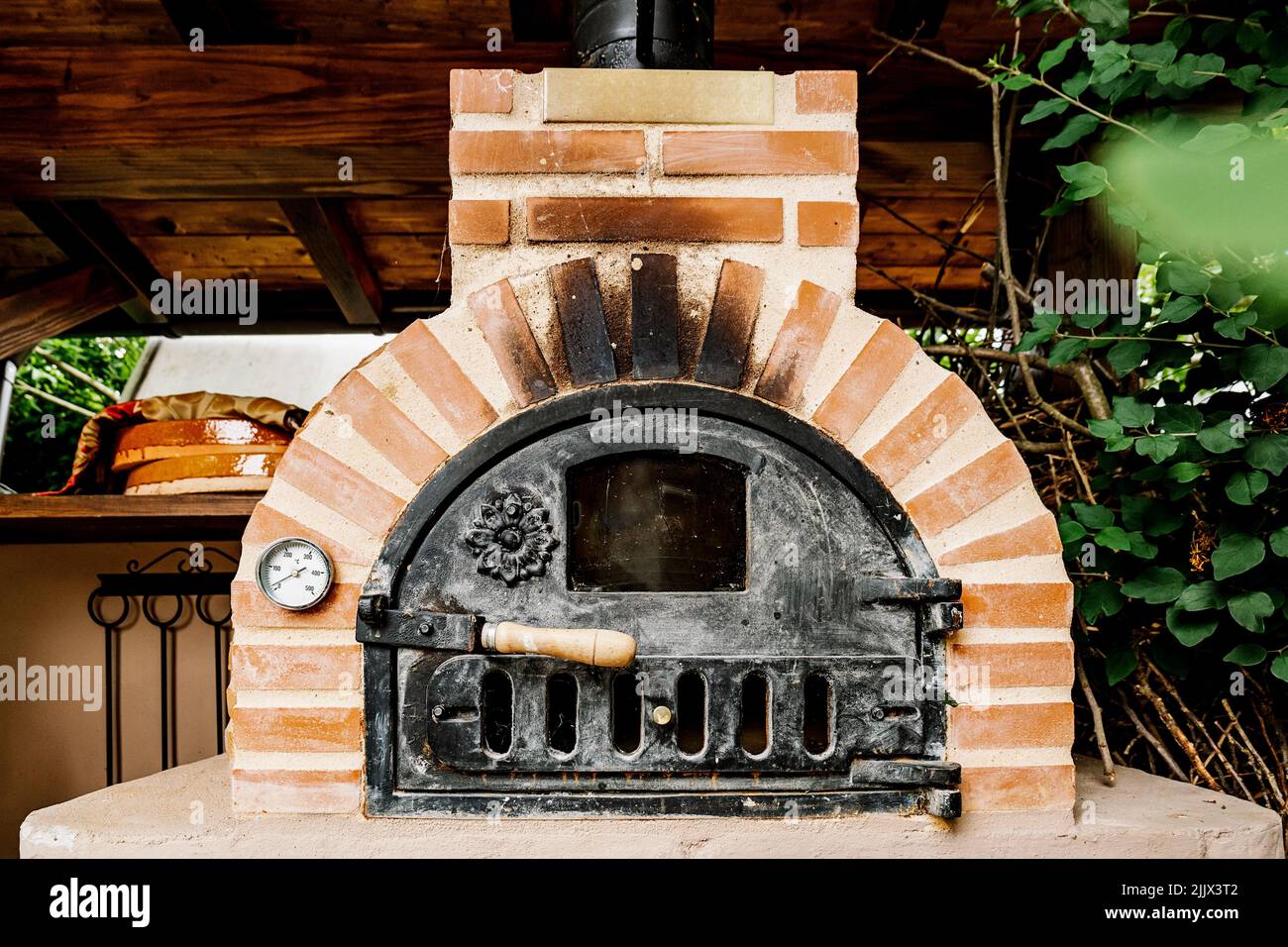 Traditional aged brick furnace with iron door located in wooden gazebo ...