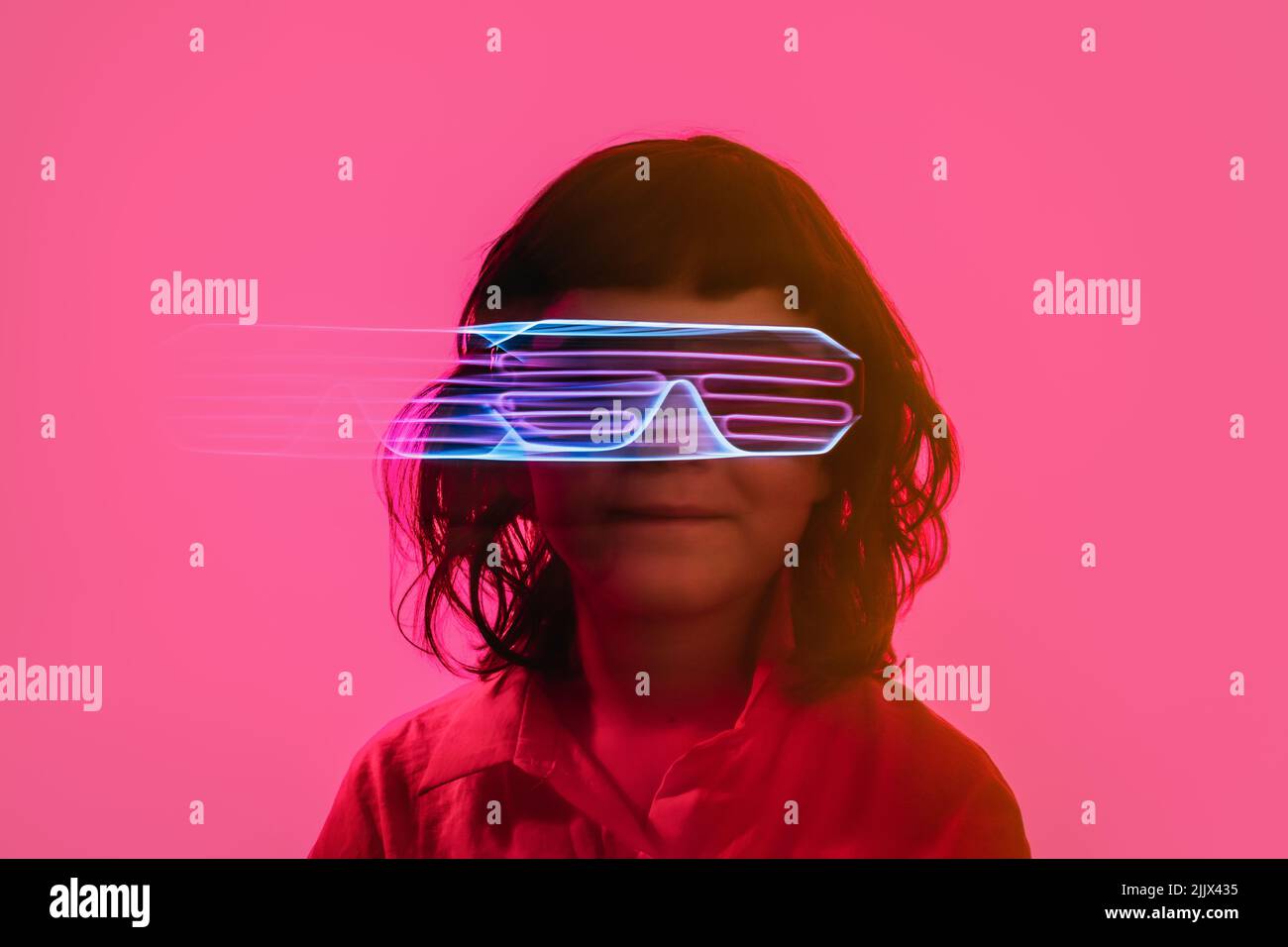Adorable little child in futuristic neon goggles during party against bright pink background Stock Photo