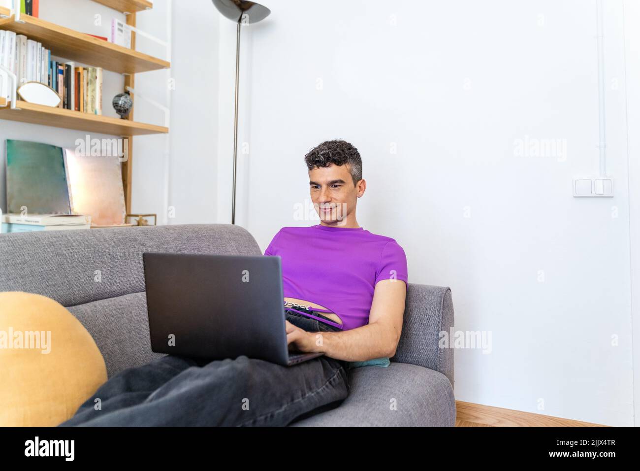 Transgender man using laptop sitting on sofa in living room Stock Photo