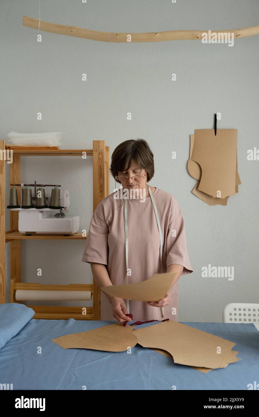 Focused professional dressmaker with measuring tape making patterns on