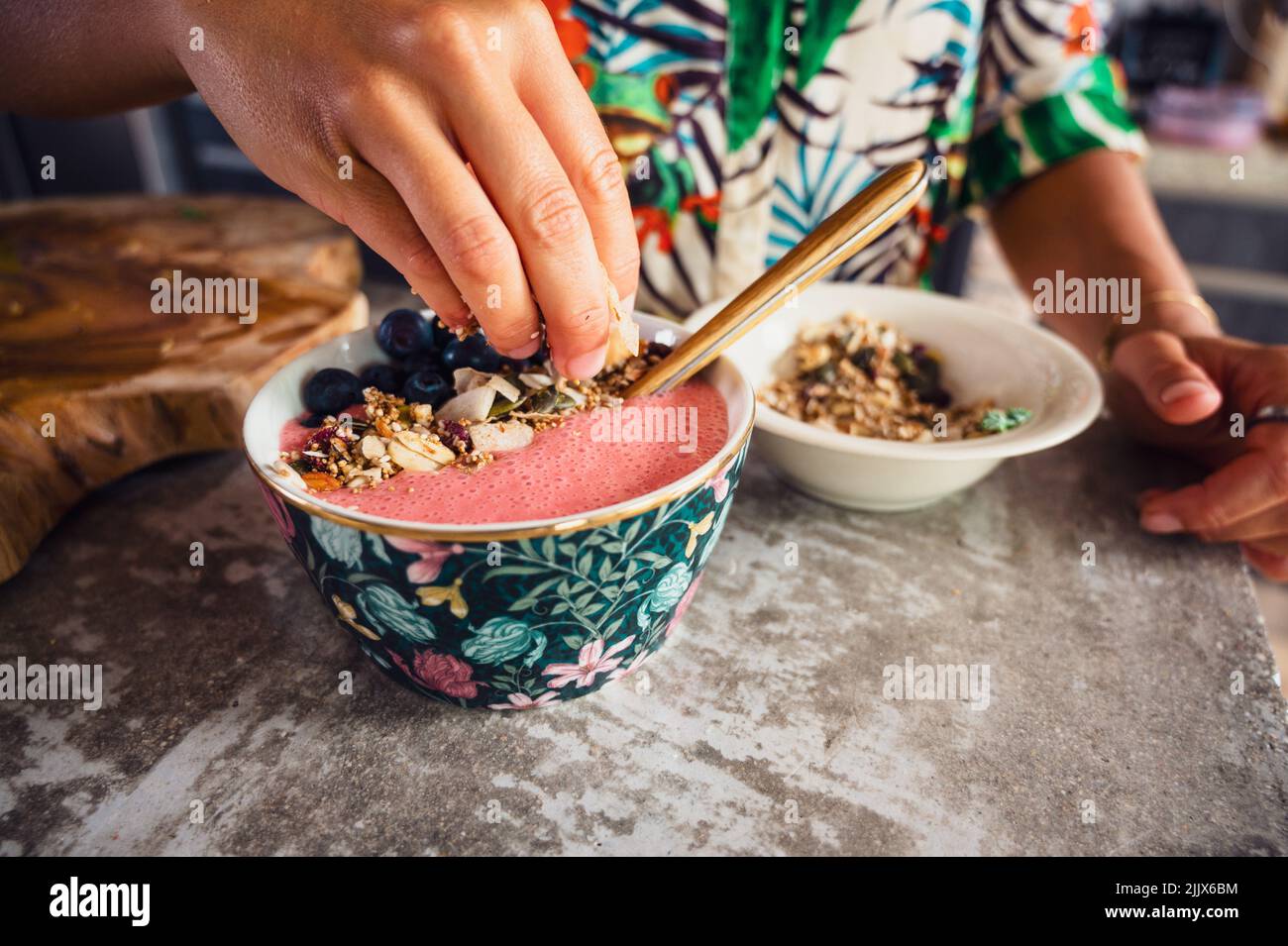 Crop anonymous female putting crunchy sweet granola into tasty pink