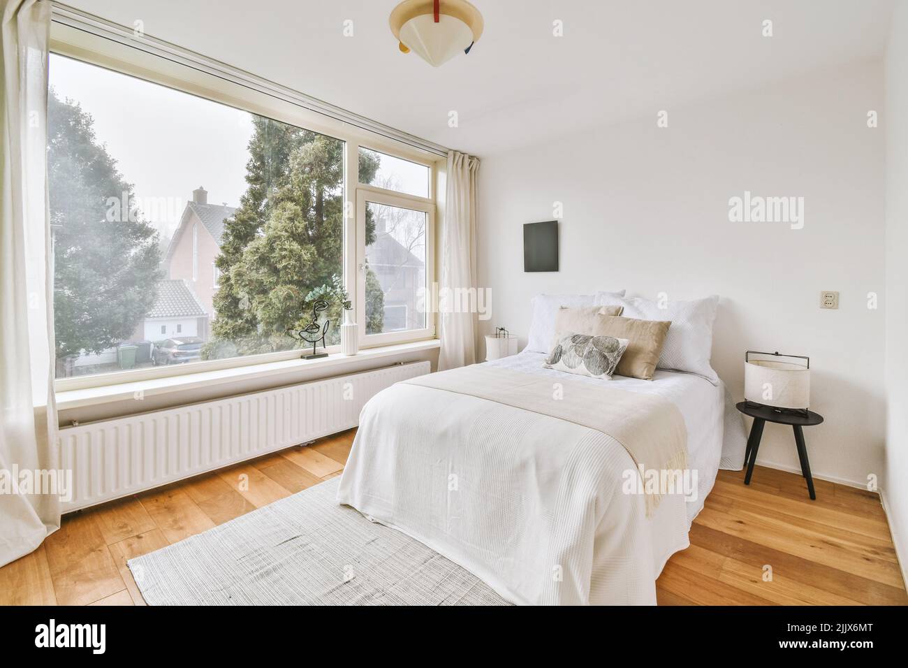 Comfortable bed next to a bright window with curtains and a wooden