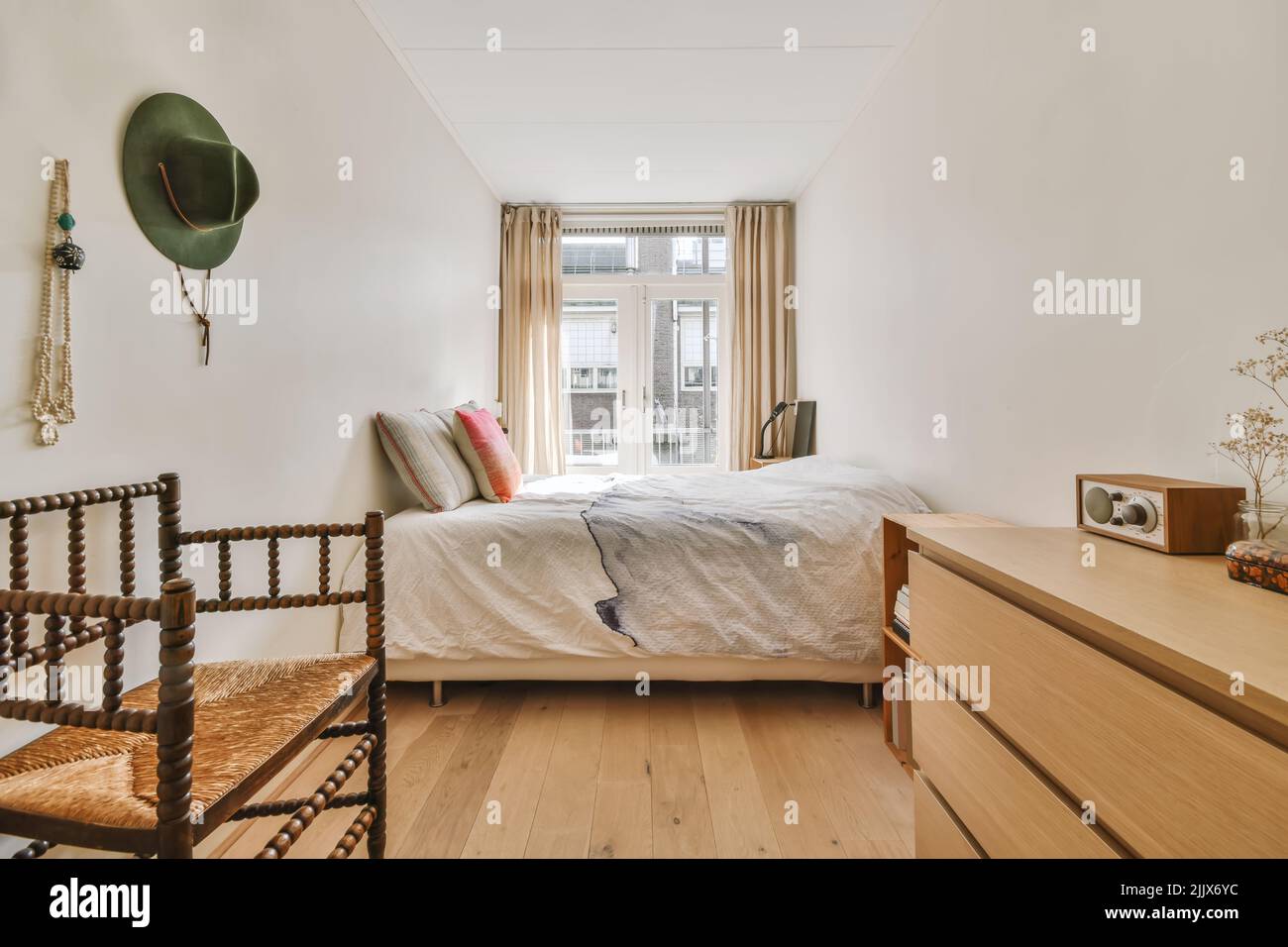 Comfortable bed with soft pillows in cozy bedroom with wooden chest of drawers and parquet floor