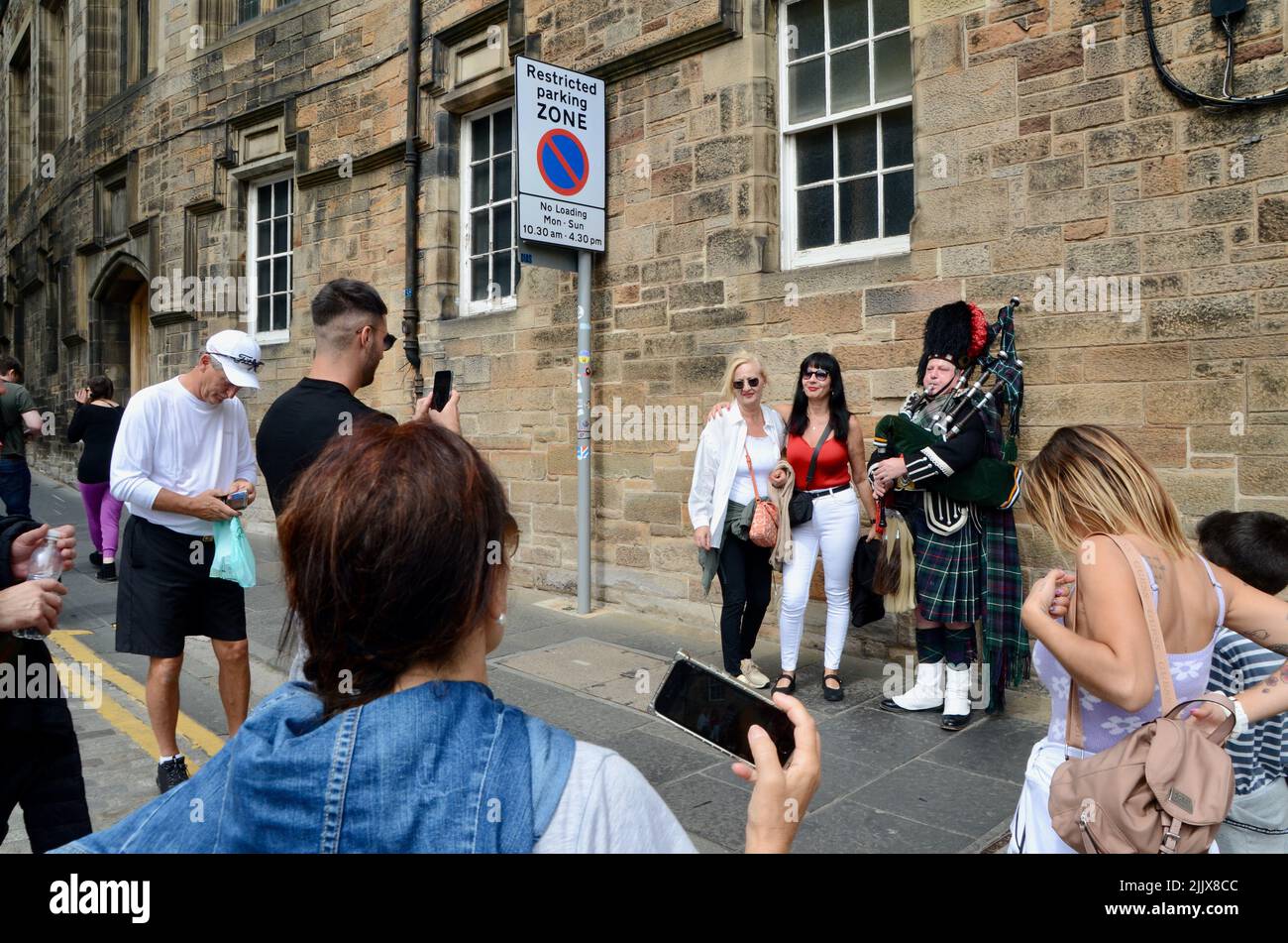 tourists pose for photos with bagpipe player in edinburgh royal mile scotland in summer 2022 UK Stock Photo