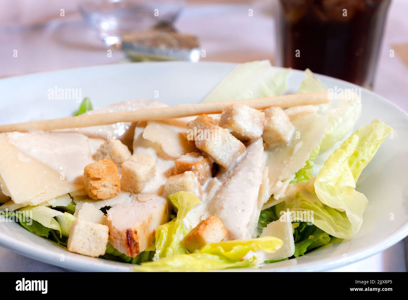 A plated, beautifully presented classic Caesar Salad served to a restaurant table. The salad is topped with a creamy sauce and croutons Stock Photo