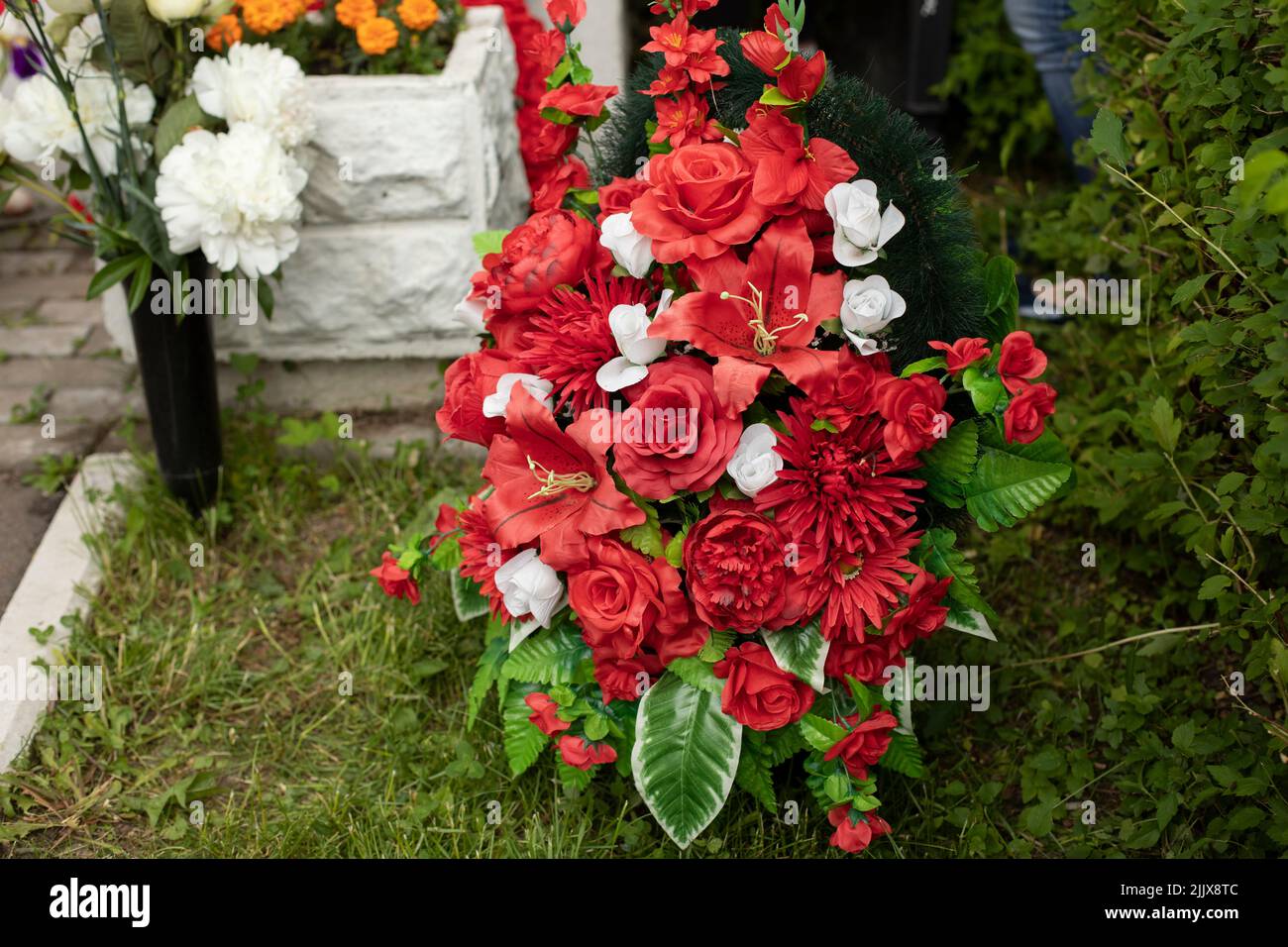 Flowers on grave of soldier. Mourning wreath. Red artificial flowers