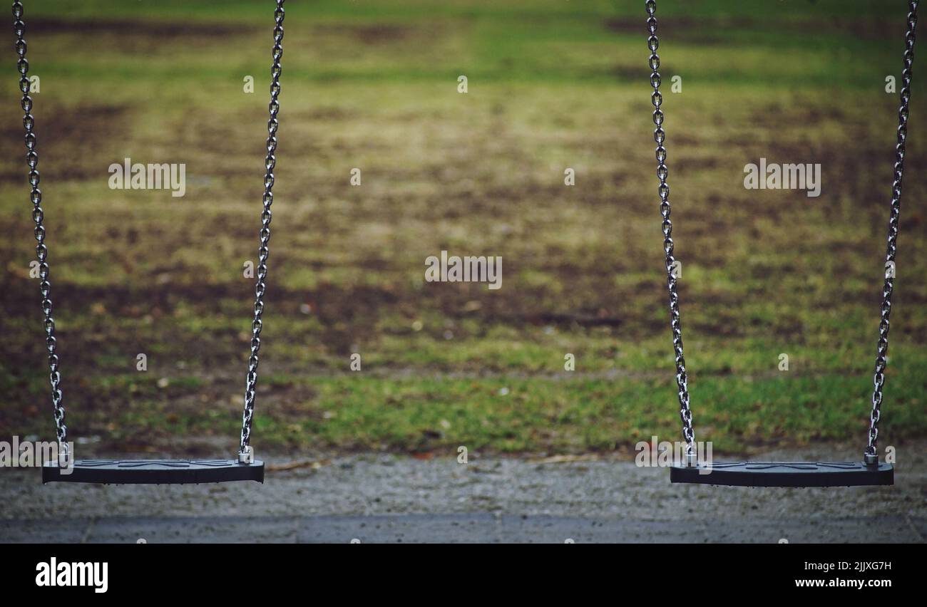 A closeup shot of two swings hanging steadily next to each other during a wet weather in a park Stock Photo