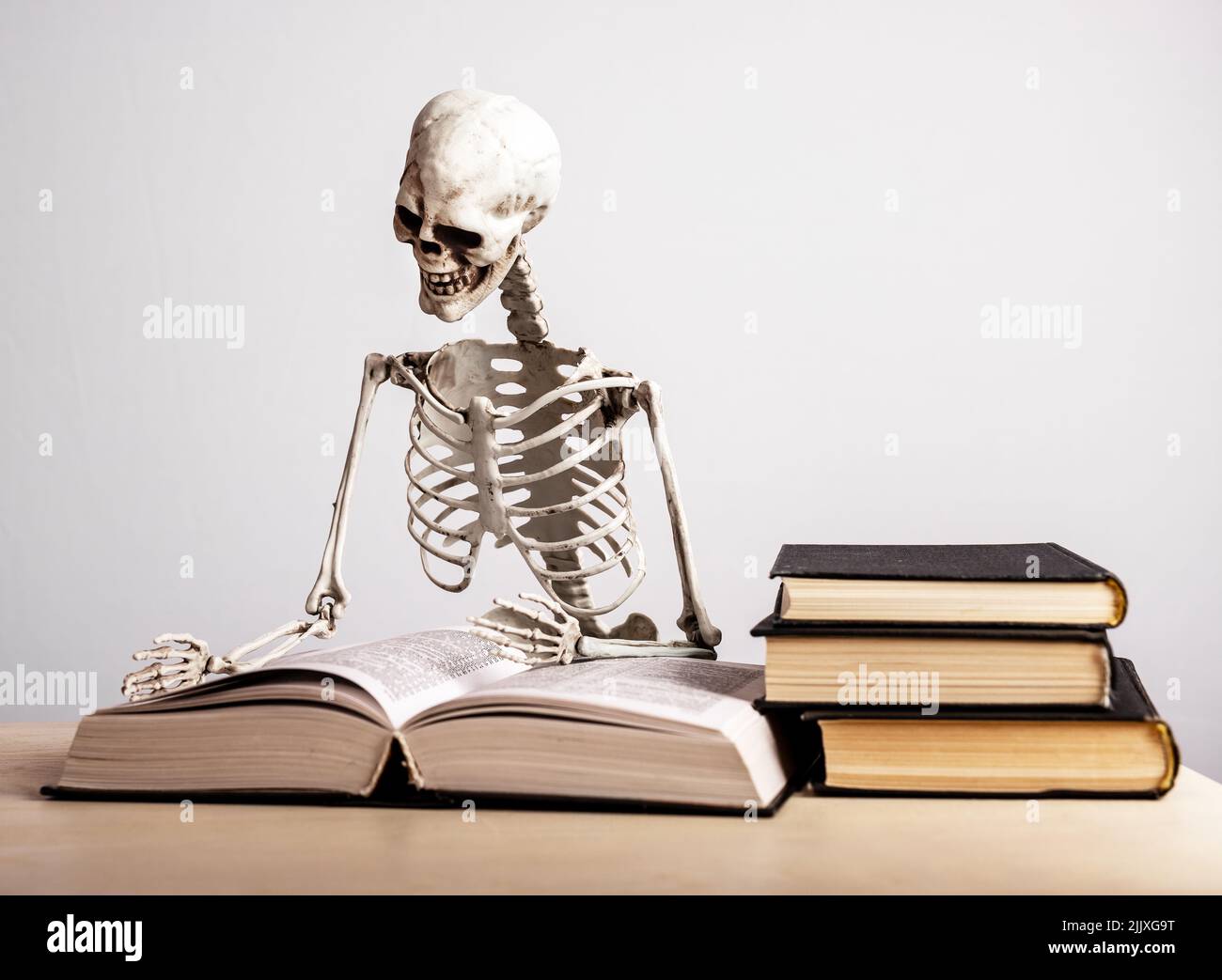 Study burnout. Skeleton sitting at table with books stack. Mental and physical exhaustion, fatigue, stress from prolonged concentration on education. Preparing for exams. High quality photo Stock Photo