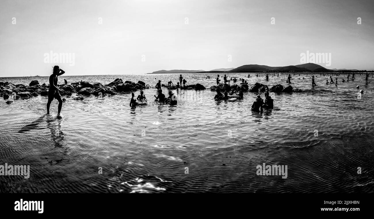 July 26th, 2022, Alghero, Italy - Black and white photo of people's silhouettes at Spiaggia di Maria Pia beach in the province of Sassari, Sardinia Stock Photo