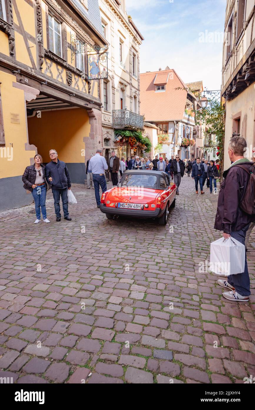 Red sports car drives through town with tourists onlooking.  Stock Photo