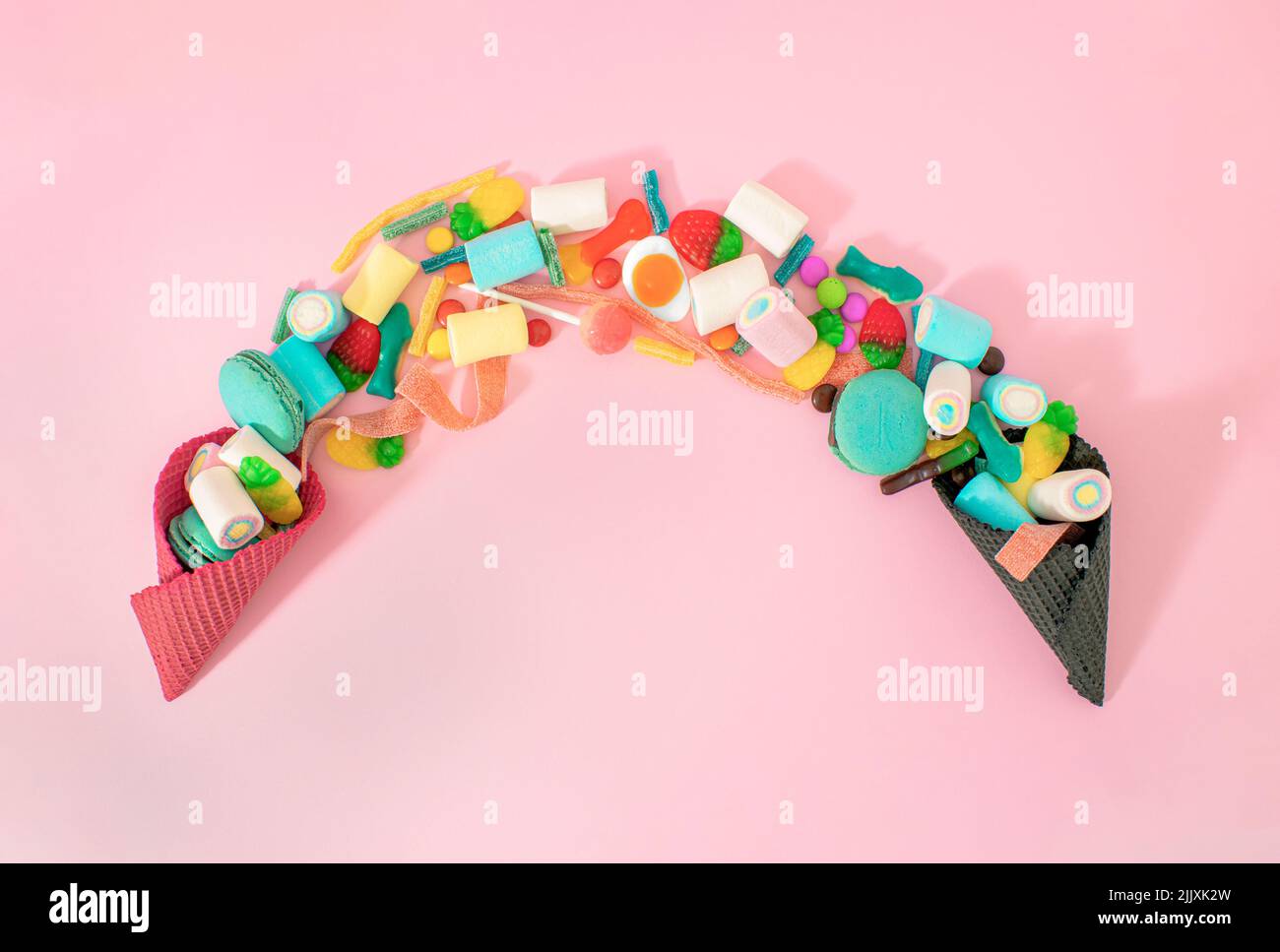 Creative junk food concept of a lots of delicious sweets in an ice cream cone on pastel pink background. Kids, are you up for a tasty candy snack? Stock Photo