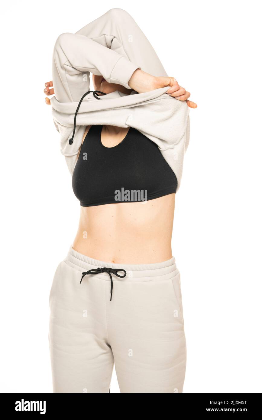 Front view of a young woman takong off her gray tracksuit and hood to a white background in the studio. Stock Photo