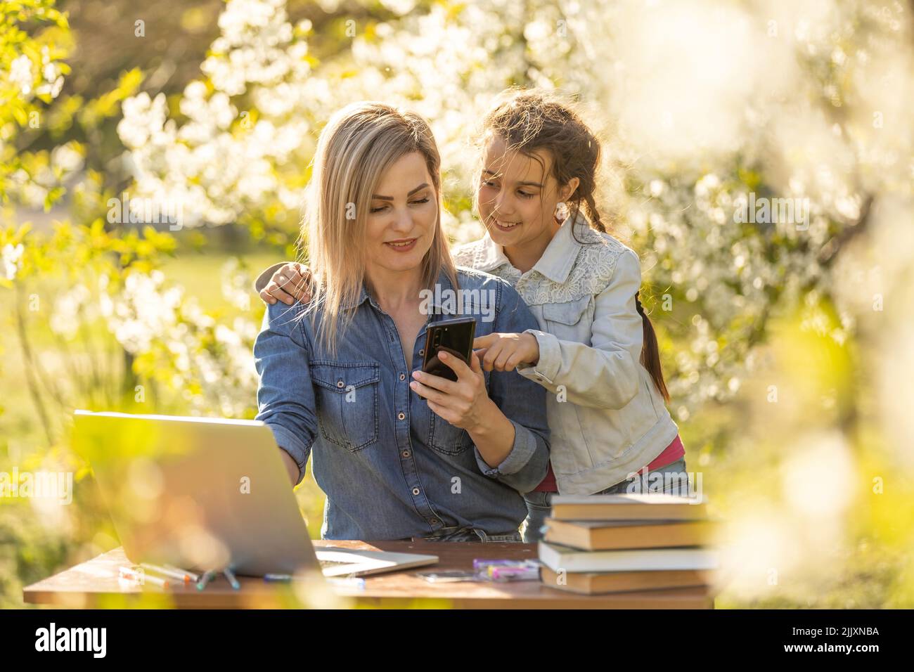 Cheerful little schoolgirl talking to the teacher while studying remotely  via laptop at home with mom nearby and giving support Stock Photo - Alamy