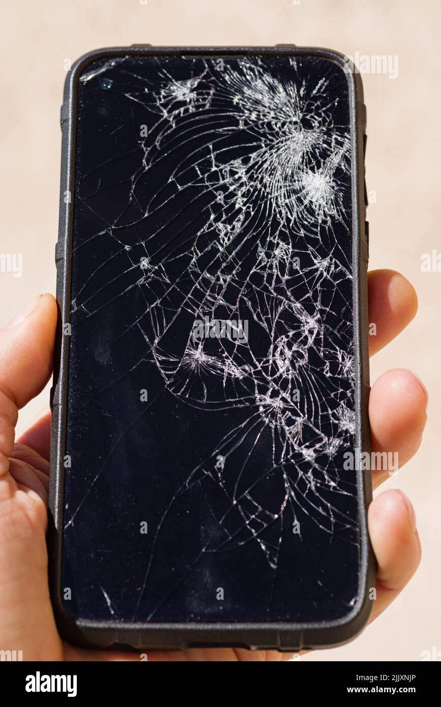 a mans hand holding a smartphone with a shattered screen Stock Photo