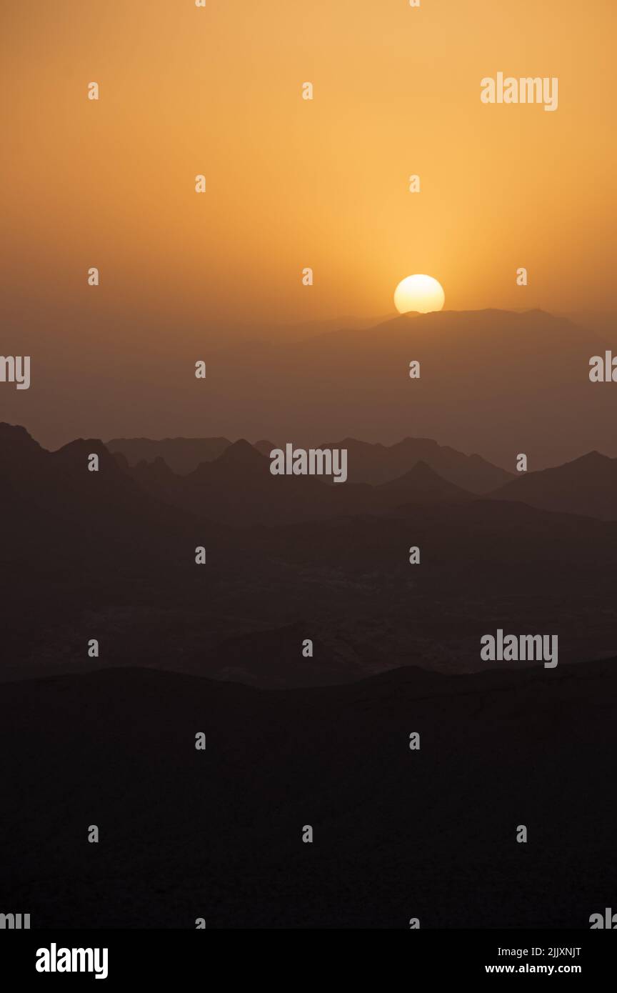 the sun sets over hazy desert mountain ridges on a windy dusty day Stock Photo