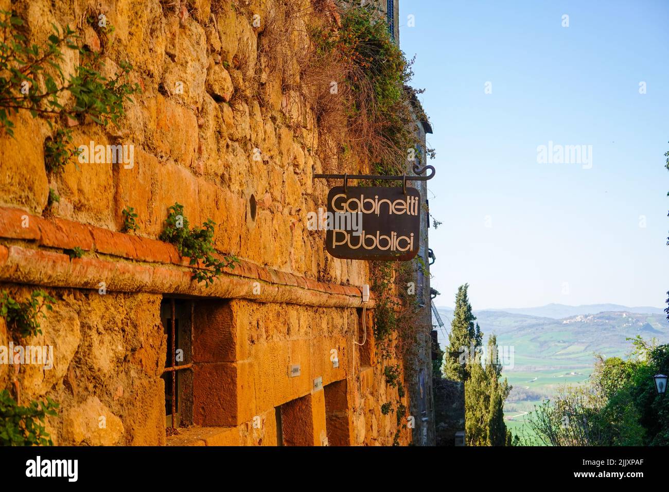 Sign on an old weathered stone building advertising the public toilets, Gabinetti Pubblici, in the Tuscan hillside town of Pienza, Italy. Stock Photo