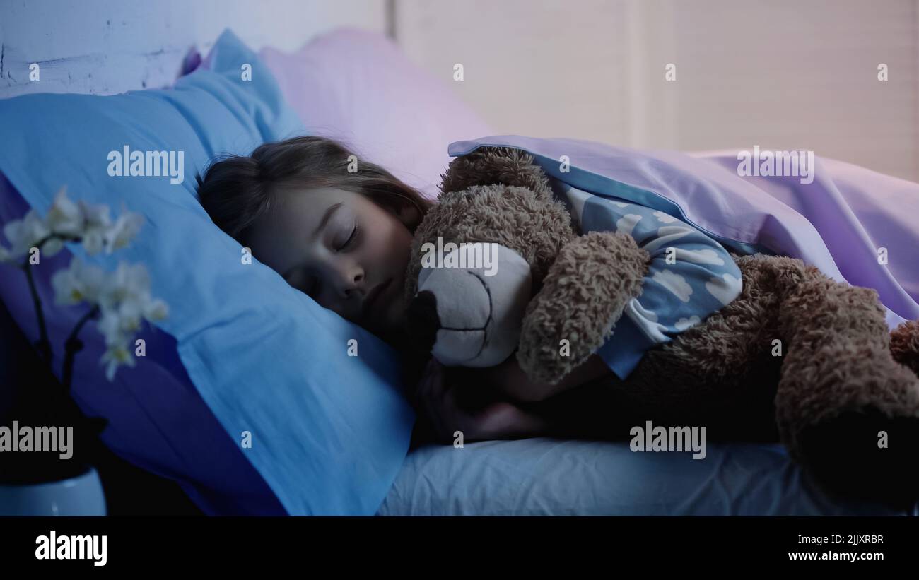 Preteen kid hugging soft toy while sleeping on bed at home Stock Photo