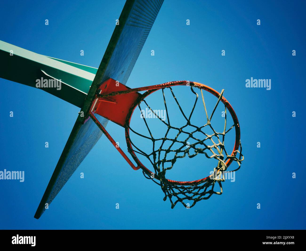 A low angle shot of a basketball hoop under the blue cloudless sky ...