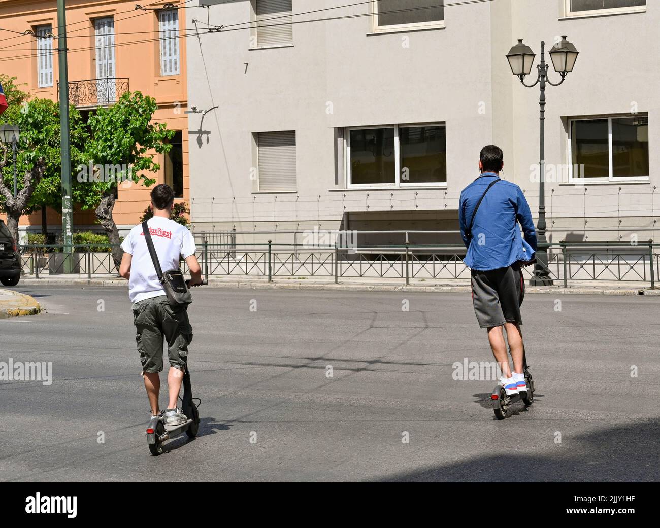 Athens, Greece - May 2022: Two young people riding electric scooters on a main road in the city centre Stock Photo