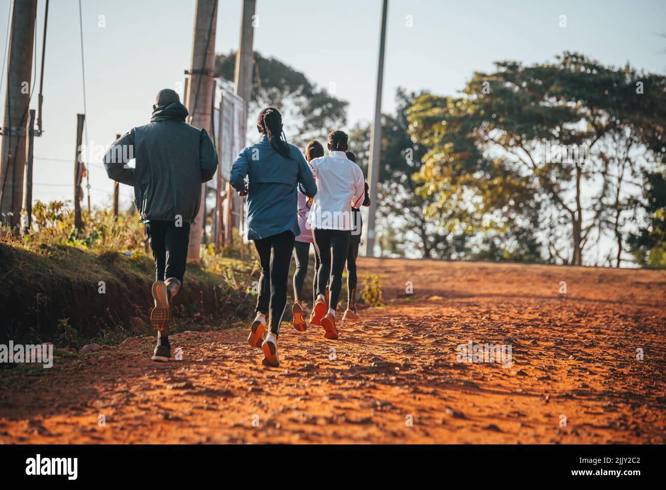 Morning running training in Kenya. A group of endurance runners run on red soil at sunrise. Morning running motivation for training. Stock Photo