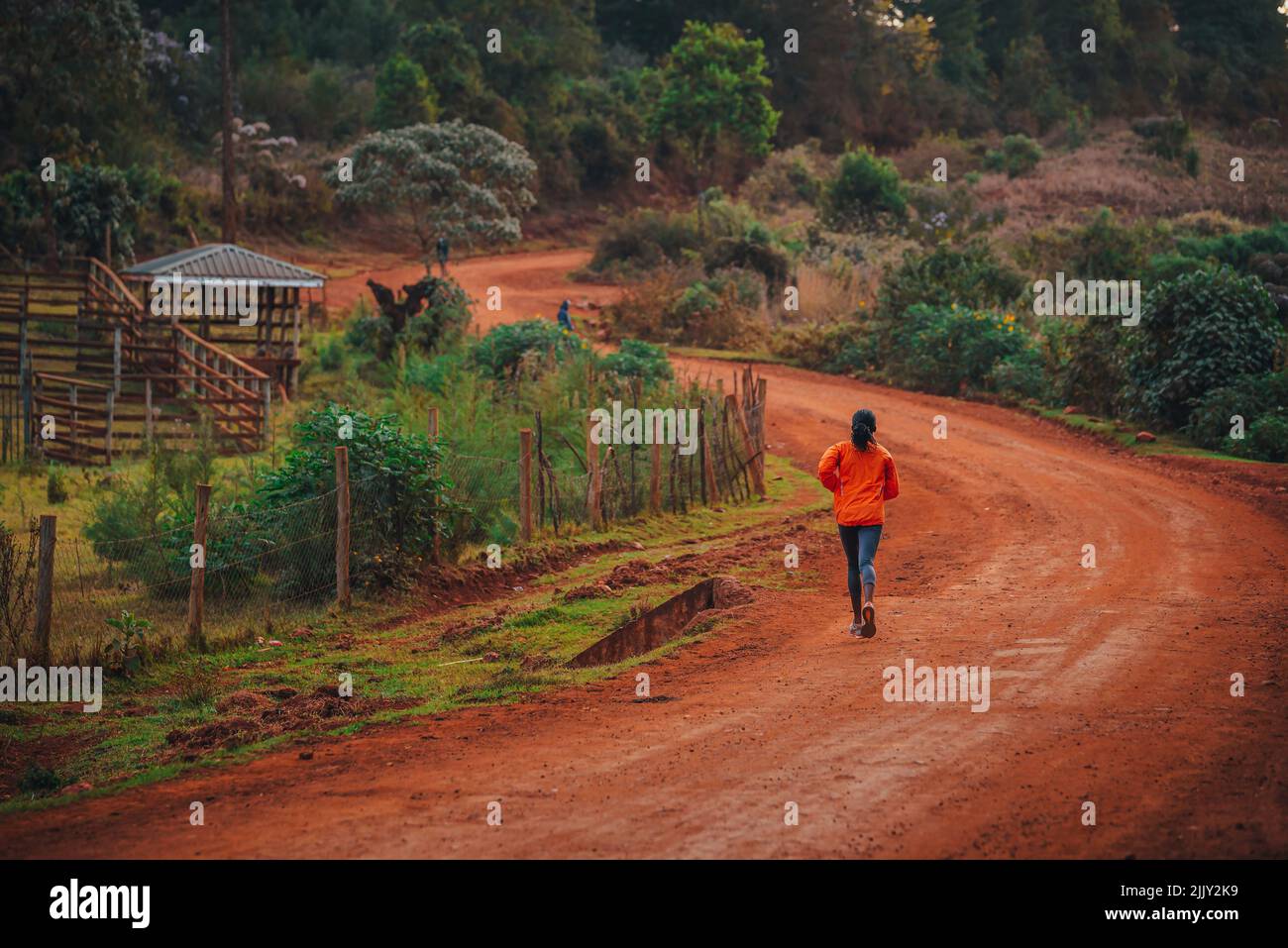 Alone Kenyan woman trains to run in Africa. A female marathon runner runs on red soil in the city of Iten, home of Champions. Stock Photo