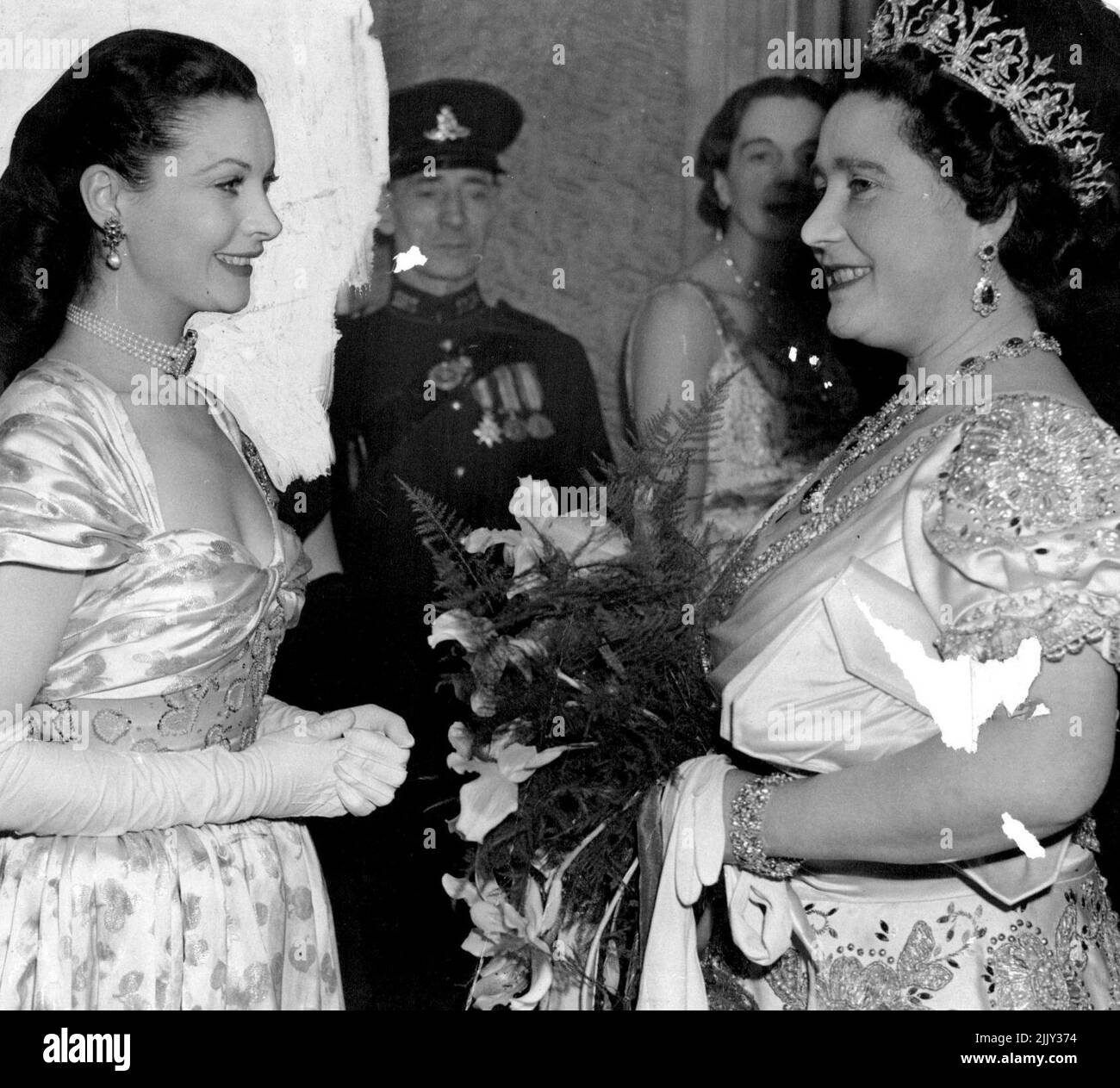 Queen, diamond tiara and ruby and diamond earrings sparkling, above her crinoline satin dress, talking with British film actress Vivien Leigh after the show. In scenes reminiscent of last year when the Royal family was nearly mobbed by film-mad crowds, a section of the huge throng broke through the 1,000 strong police cordon in Leicester Square London, and brought the Royal family's car to a halt as they arrived for the Royal Command Film Show at the Odeon Theatre. Police quickly cleared a path for the car and the King and Queen with Princess Margaret, drove on to the Odeon. November 25, 1947. Stock Photo