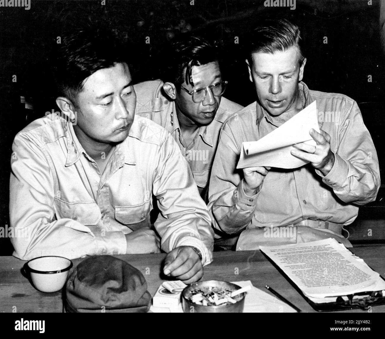 ROK Delegate Hears Translations - Maj. Gen. Paik Sun Yup, (left), ROK delegate to the UN coaso fire talks listens as Lt. Horace Underwood, USN (right) reads a translation at a nightly briefing session at Base Camp, Advance Headquarters, after a day session with communist delegates at Kaosong. Lt. Col. Lee, ROK, side to Gen. Paik, listens attentively. Lt. Underwood is one of the principal interpreters at the talks, handling great volumes of North Korean language translations. August 15, 1951. (Photo by U.S. Navy photo). Stock Photo