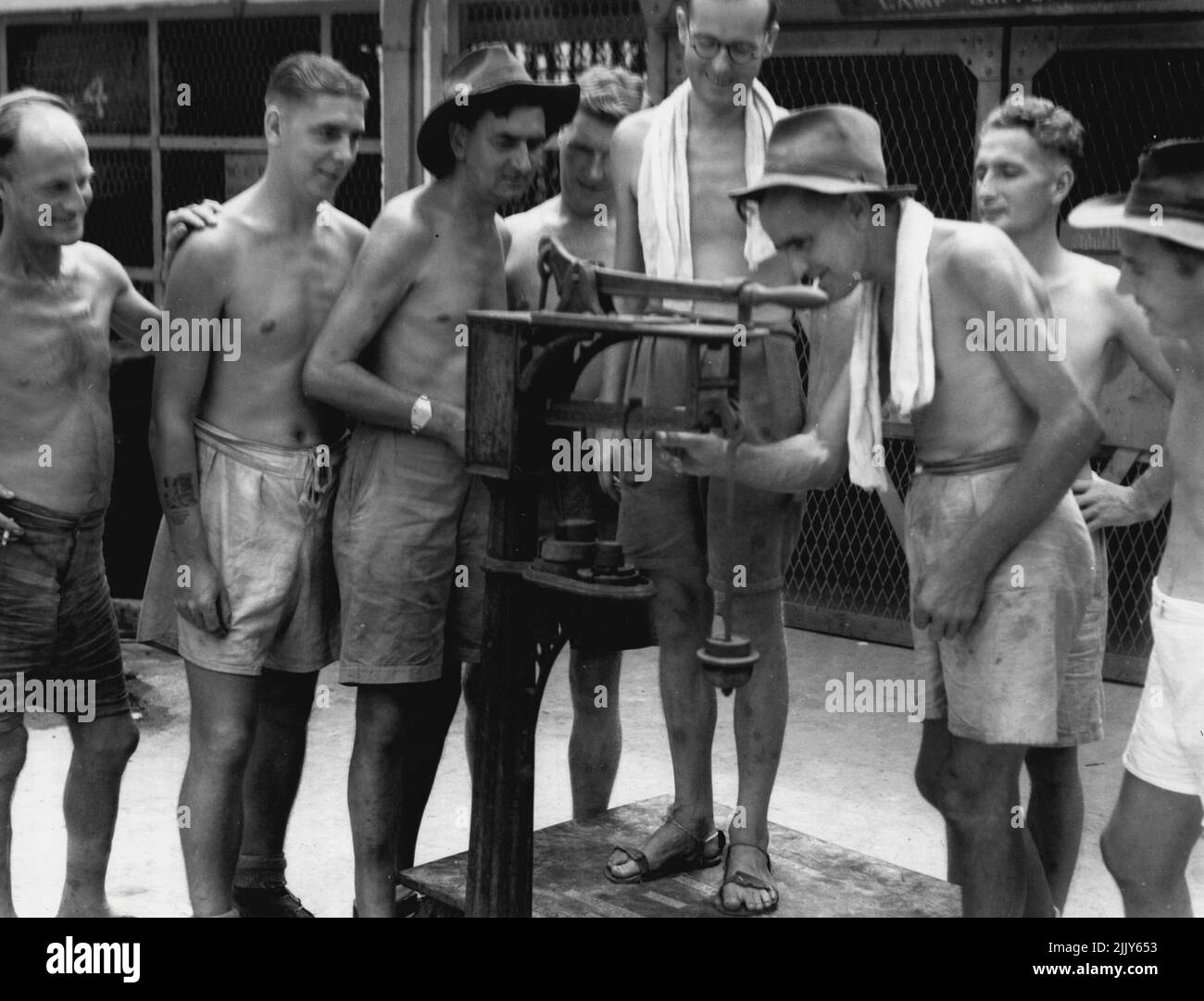 Members of 8 Division, ex prisoners of war of the Japanese, checking their weight gains on a set of scales in the jail courtyard. September 19, 1945. (Photo by Australian War Memorial Canberra). Stock Photo