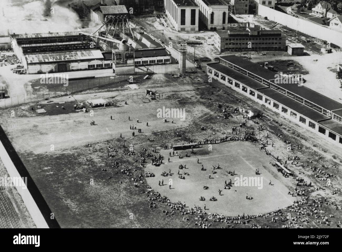 Rioting Prisoners Quieted - While three build- inside the wall of Oregon's State Prison burned, rebellious convicts watch from the baseball diamond, where they were herded by guards. The burning flax plant is shown in upper left. July 21, 1953. (Photo by AP Wirephoto). Stock Photo