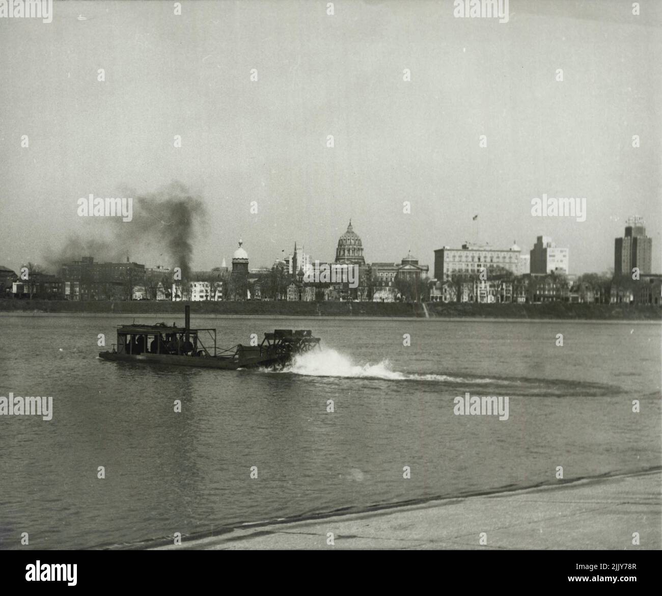 End of an Era - Framing Pennsylvania's Capitol Buildings in black smoke and white wash, a paddlewheel barge churns up the Susquehanna River, en route to the underwater coal beds that have been dredged clean of the fuel. March 26, 1954. (Photo by United Press). Stock Photo