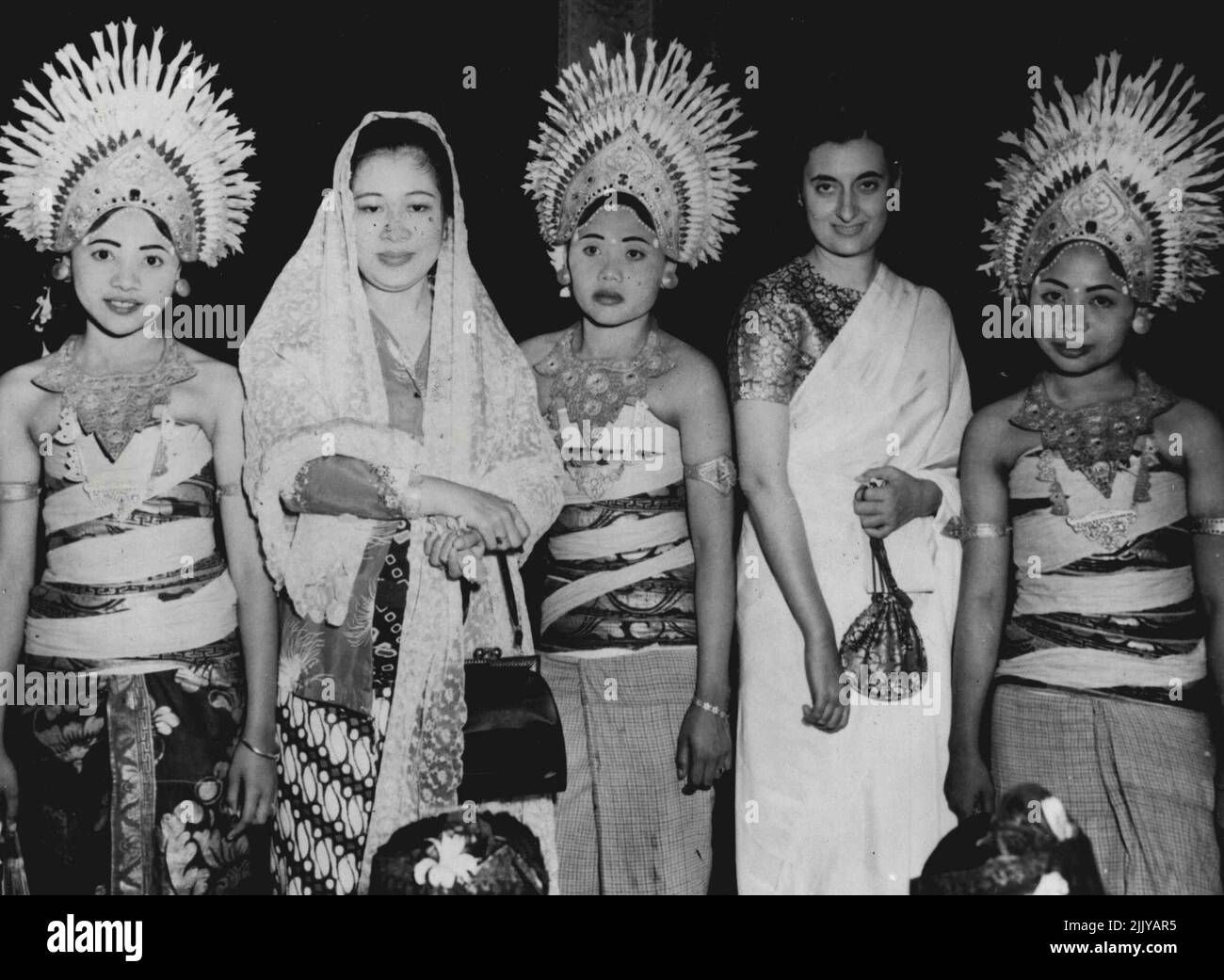 Dancing girls of the Island of Bali wear flower-topped headdresses of gold as they frame the wife of President Soekarno of Indonesia (left) and Mrs. Indira Gandhi, daughter of Premier Jawaharlal Nehru of India (right), during the state visit made to Indonesia by Nehru in mid-June. June 22, 1950. (Photo by Associated Press Photo). Stock Photo