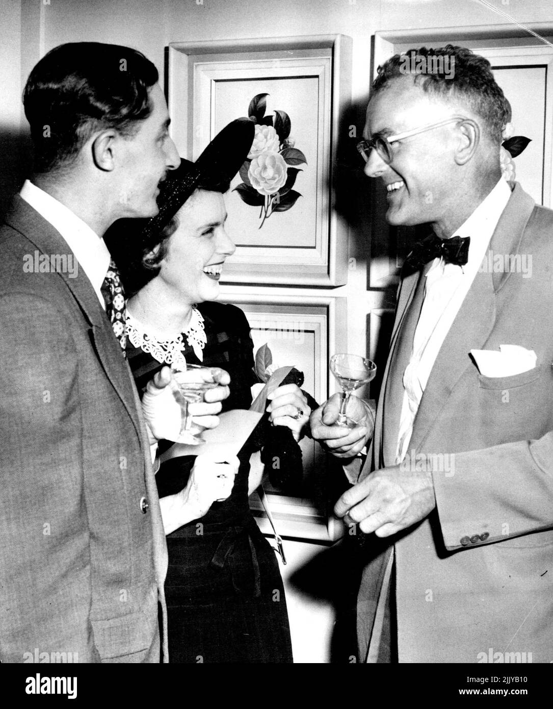 Mr. Sam Ure Smith, who published Camellia Trail discusses the exhibition with his wife and National Art Gallery director Hal Missingham. Mrs.Ure Smith's dress is black sheer cotton and she has added a large black lacquered straw hat. December 19 1952. Stock Photo