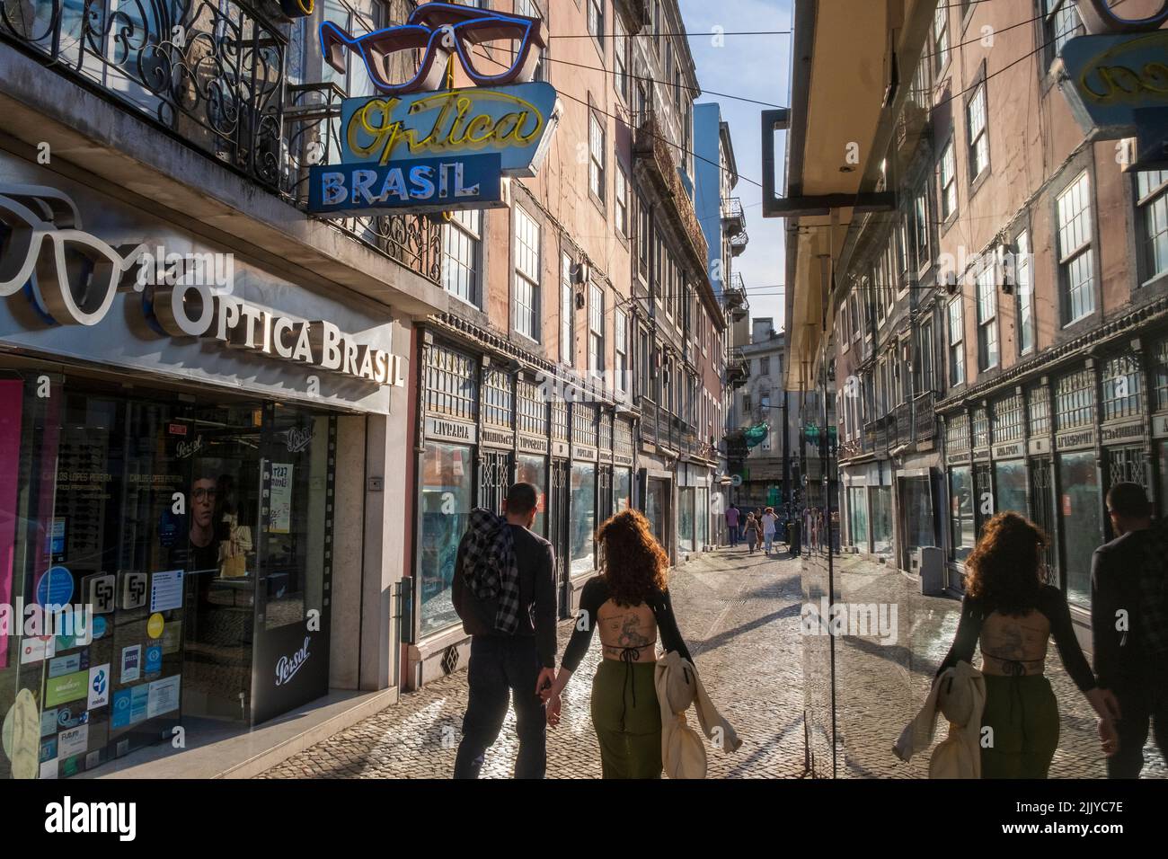 A couple walking, businesses reflected in a window, Lisbon, Portugal Stock Photo