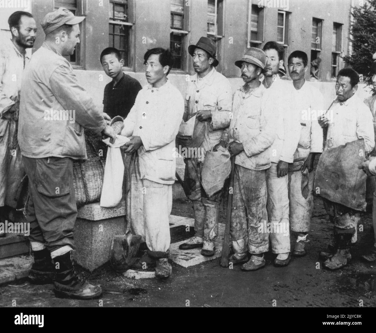 Korean Laborers Paid Off In Rice -- M/Sgt. Robert J. Ross, USMC, of Santa Ana, Calif., pays Korean laborers employed by the Marines at the Wonsan airstrip in North Korea with rice, the accepted form of payment. The Korean workers are used to help clear the field. November 11, 1950. (Photo by AP Wirephoto). Stock Photo