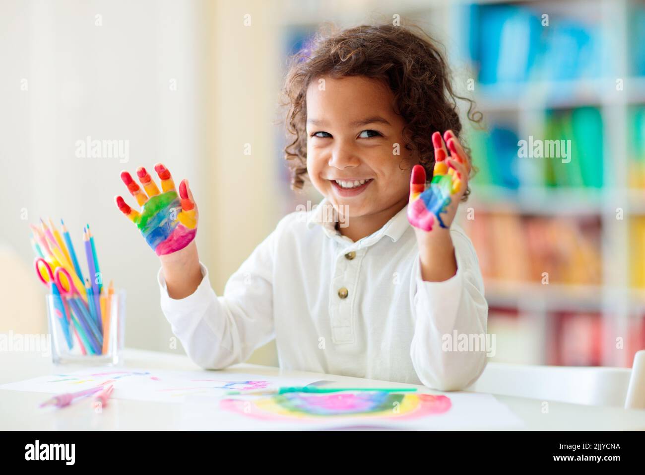 Child drawing rainbow. Paint on hands. Remote learning and online school art homework from home. Arts and crafts for kids. Stock Photo