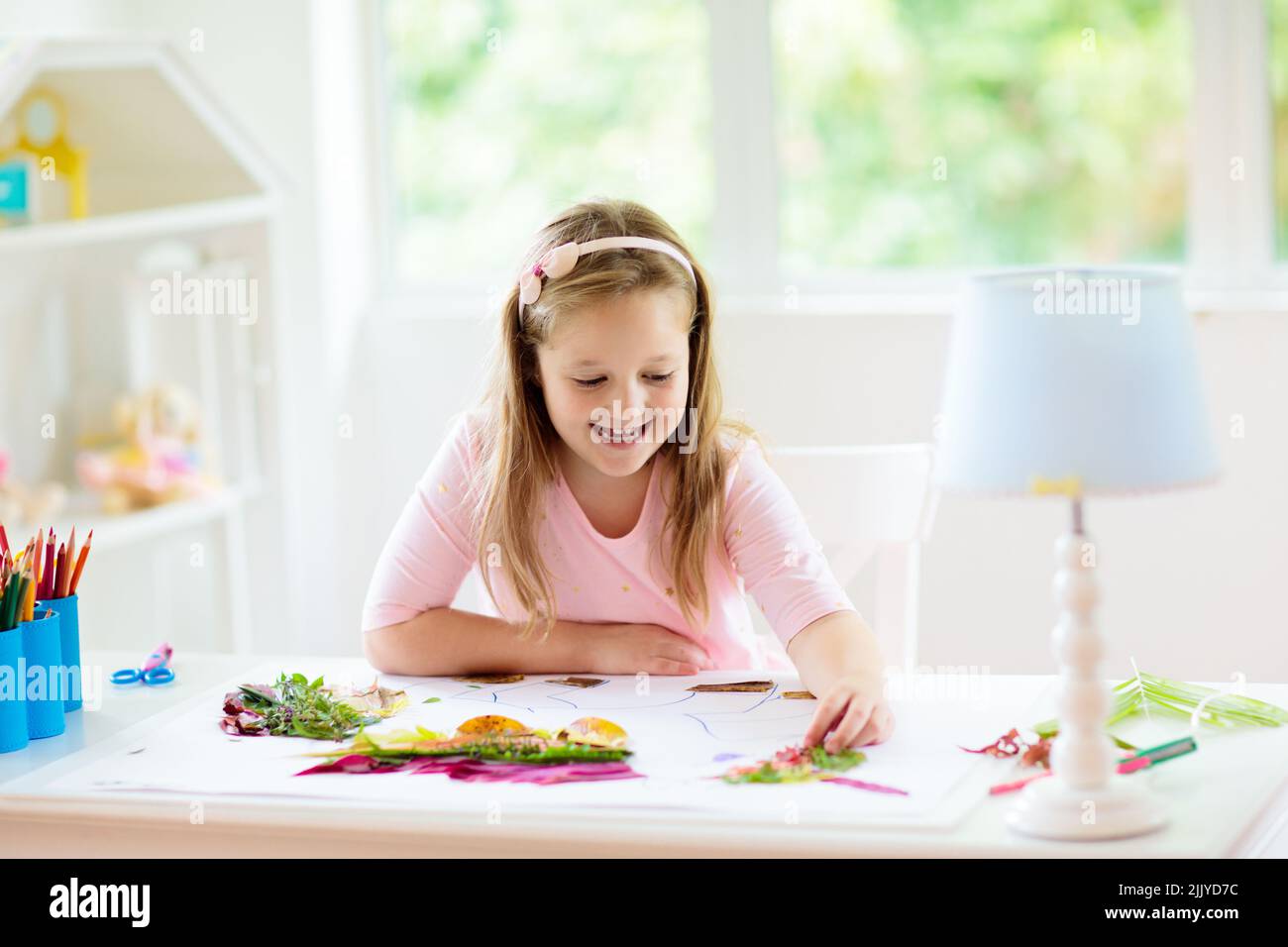 Child creating picture with colorful leaves. Art and crafts for kids. Little girl making collage image with rainbow plant leaf. Stock Photo