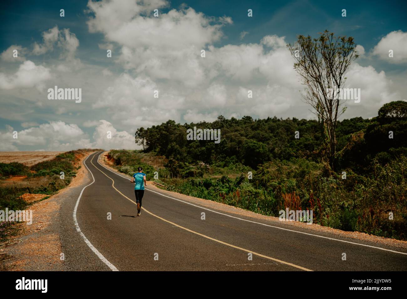 Endurance runner running on asphalt road in African nature. Marathon training in Kenya Stock Photo