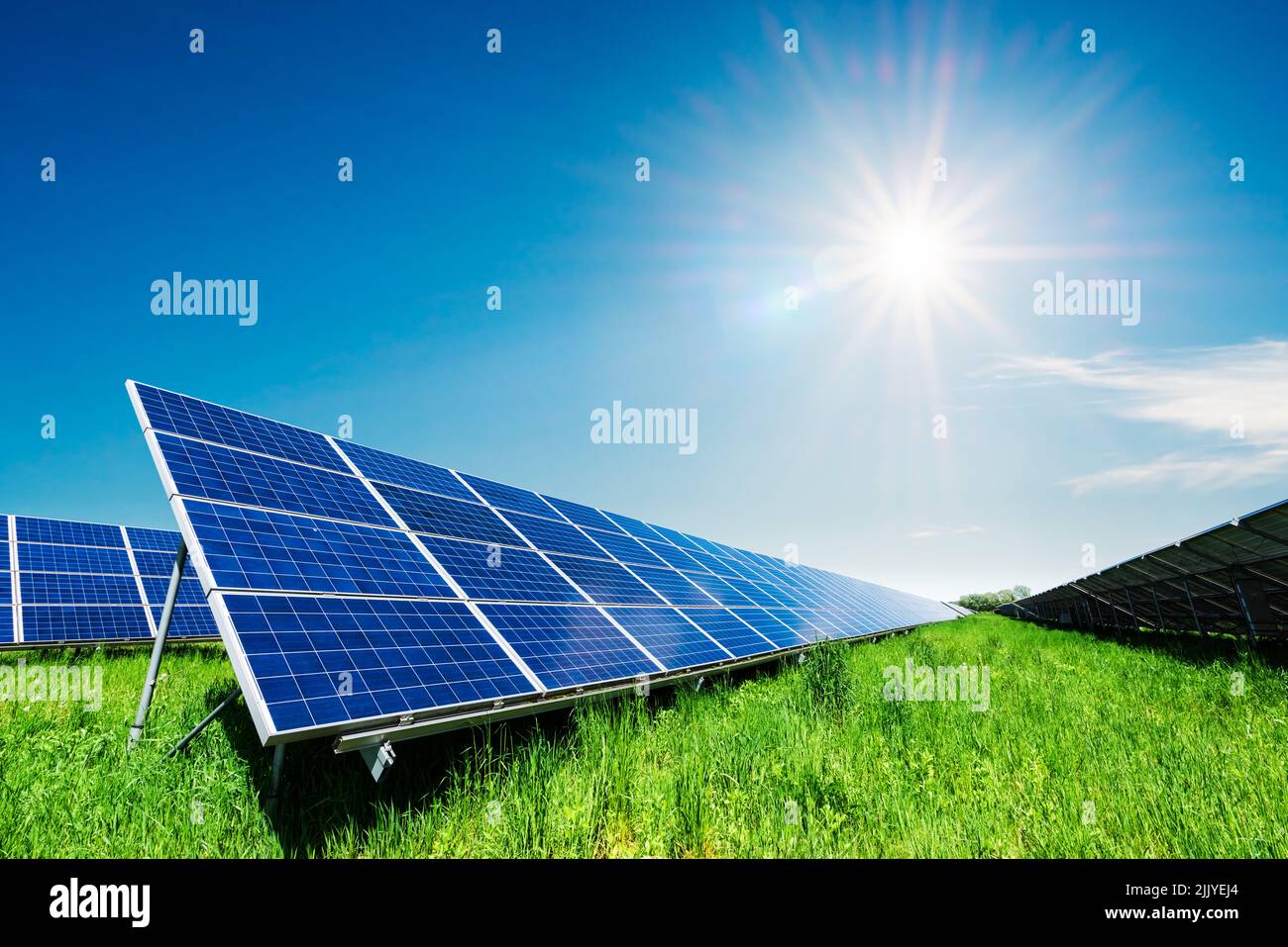 Solar panel under blue sky with sun. Green grass and cloudy sky. Alternative energy concept Stock Photo