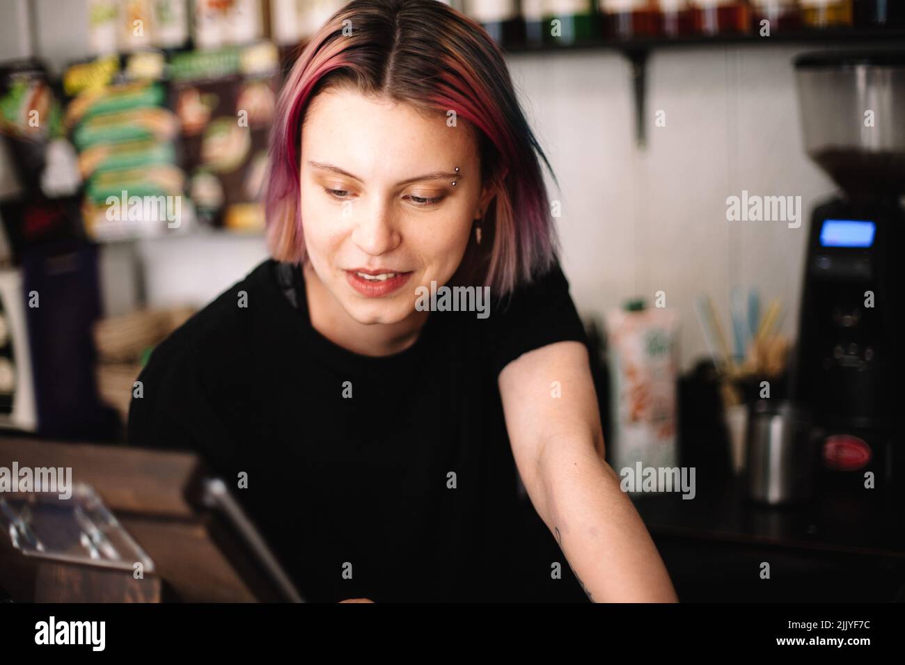 Happy young female barista working at checkout counter in coffee shop Stock Photo