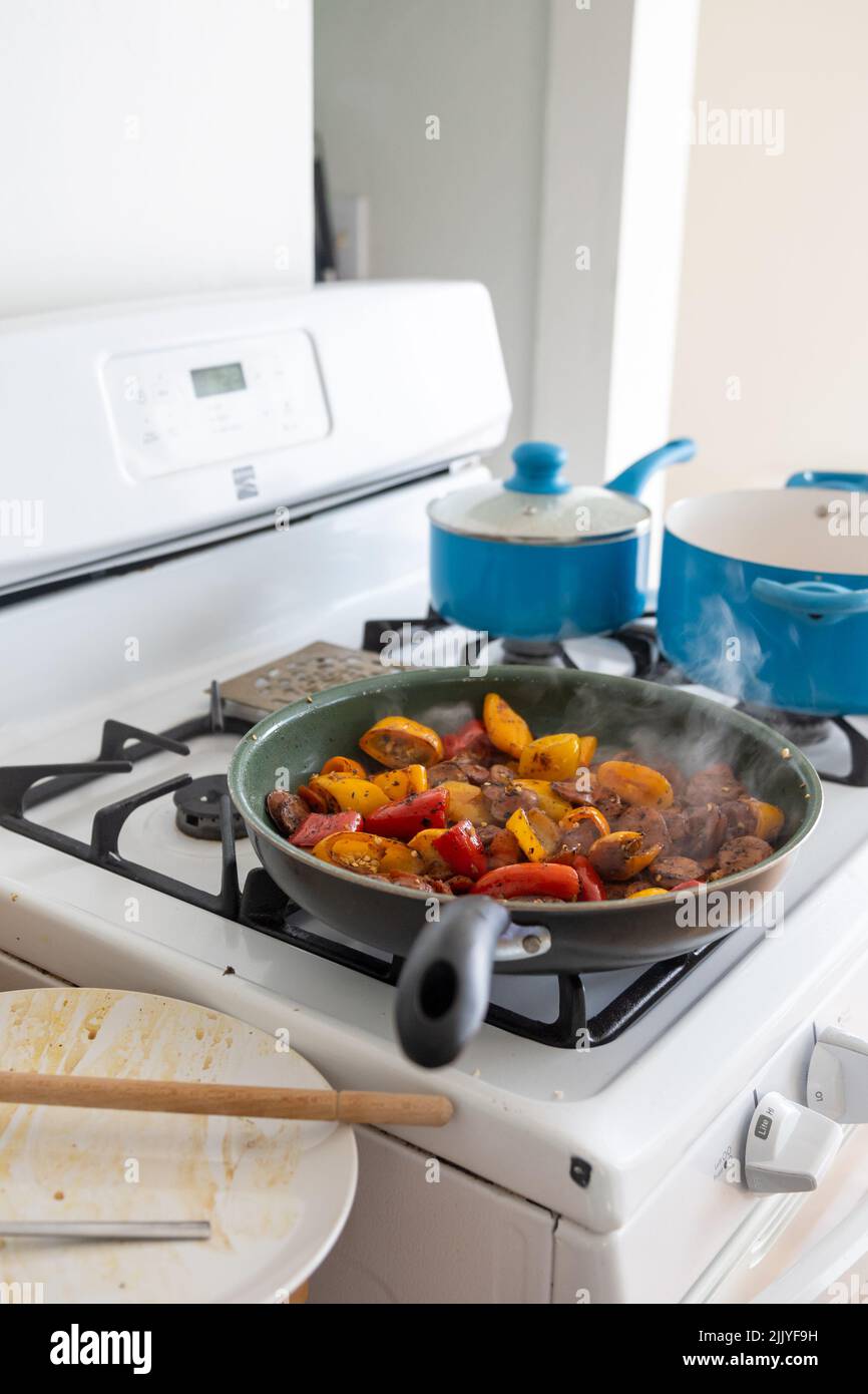 Roasting peppers and zucchini vegetables on non-stick pan on white stovetop while cooking two other items on blue pans- healthy meal home cooking conc Stock Photo